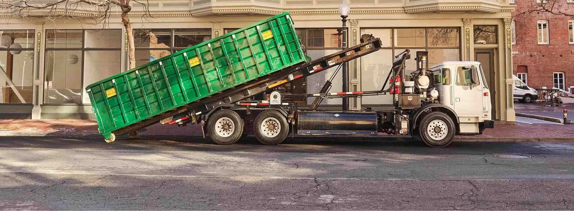 Waste Cost Solutions roll-off truck delivering a green dumpster on site